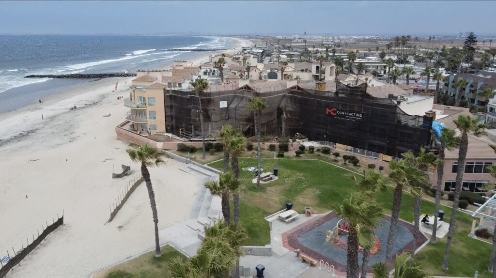 Coastal resort with beach, palm trees, and buildings near the ocean.